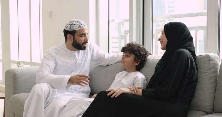 Happy Muslim parents talk to little cute son spend time together at home. Loving mom and dad in traditional clothes enjoy pleasant conversation to their kid boy. Family ties, communication, upbringing Royalty-Free Stock Footage #1108437871