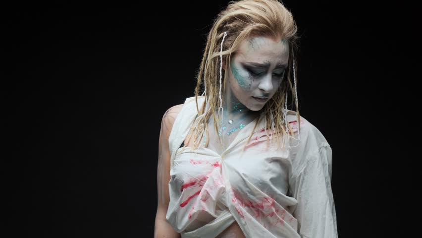 Halloween woman in makeup and a white shirt stained with blood in the studio on a black background.