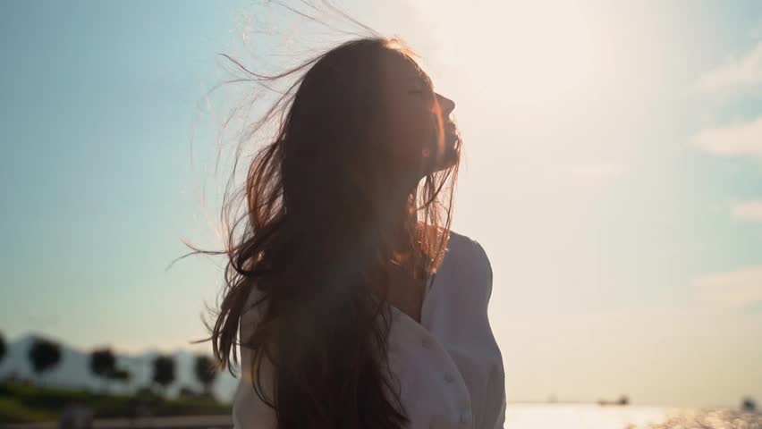 Relaxed girl woman breathing fresh air raising arms over sunset sky at summer seaside. Dreaming, freedom and traveling concept. Female mental health wellness