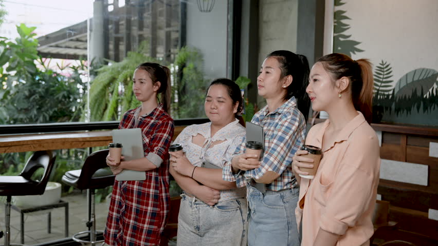 Group of female office workers, Asian women close friends Smiling standing in the middle of a coffee shop Have a laptop computer in hand. and holding a paper cup and coffee Smiled happily when met. Royalty-Free Stock Footage #1108446977