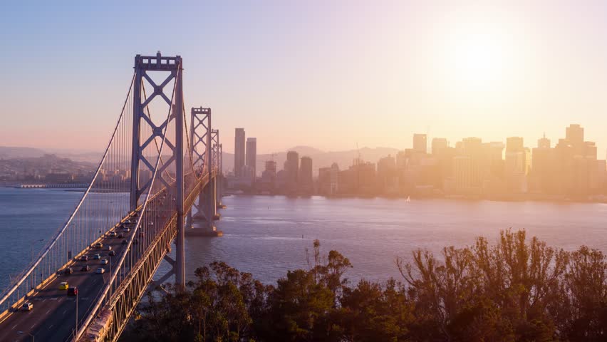 Traffic driving across the Bay Bridge in San Francisco at sunset. The buildings of San Francisco can be seen in the distance. Royalty-Free Stock Footage #1108454825