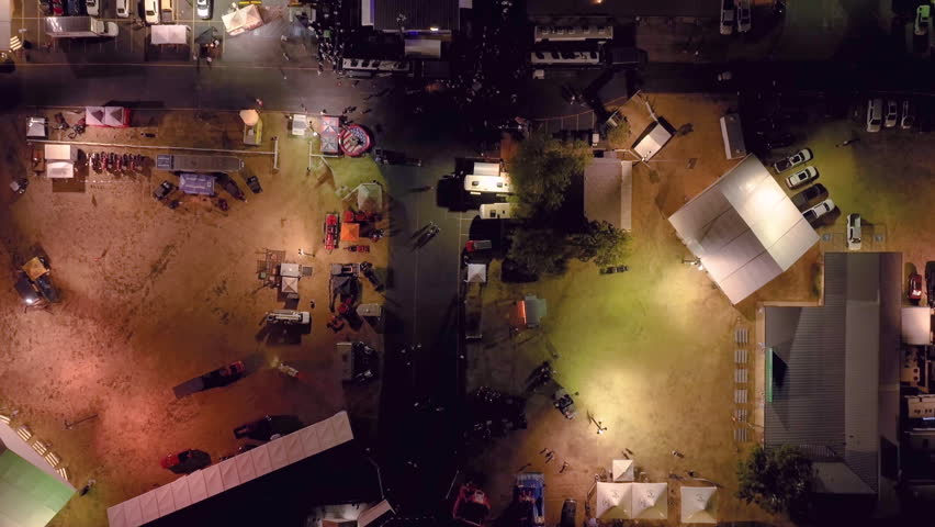 Aerial drone overhead view of a large crowd at a country music live concert at a state fair festival at night as a rodeo rink is revealed next to a colorful carnival with rides and neon lights. | Shutterstock HD Video #1108457997