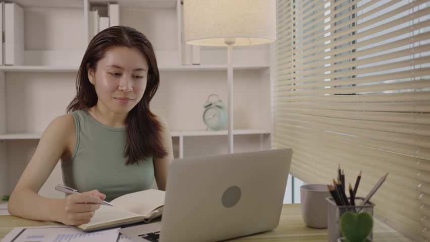 Beautiful young asian woman watching live video or video call of teacher teaching on laptop in her home, Take notes of important conversations and messages during the teacher's teaching. Royalty-Free Stock Footage #1108458235