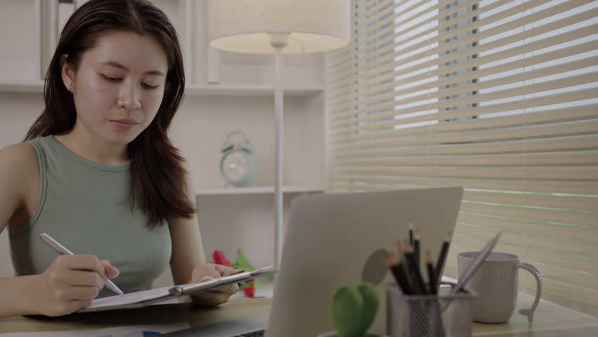 Beautiful young asian woman watching live video or video call of teacher teaching on laptop in her home, Take notes of important conversations and messages during the teacher's teaching. Royalty-Free Stock Footage #1108458243