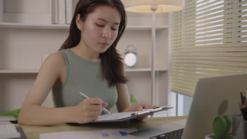 Beautiful young asian woman watching live video or video call of teacher teaching on laptop in her home, Take notes of important conversations and messages during the teacher's teaching. Royalty-Free Stock Footage #1108458253