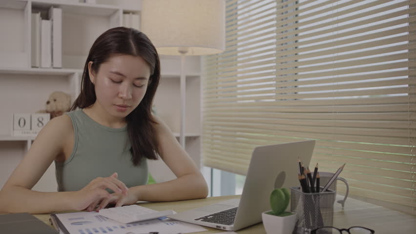 Asian woman working at home, Press the calculator to calculate the income - expenses of the house and use the laptop to record the information and check the accuracy, Home lifestyle. Royalty-Free Stock Footage #1108458257