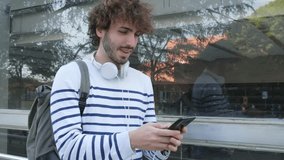 Slow motion video of young male college students standing outdoors putting on headphones to listen to music using phone.