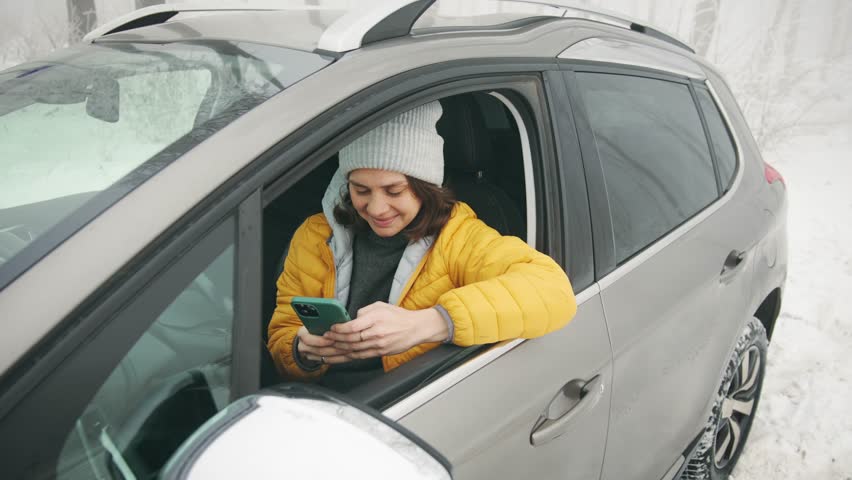A young Caucasian woman using her phone while sitting in the driver's seat of a car parked in a snowy winter forest. Royalty-Free Stock Footage #1108465107
