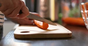 Woman's hands are slicing carrot with a knife on wooden cutting board