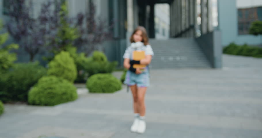 Close up of beautiful girl with school bag and books standing near school building, posing and looking at camera after classes, outdoors. Education and children concept