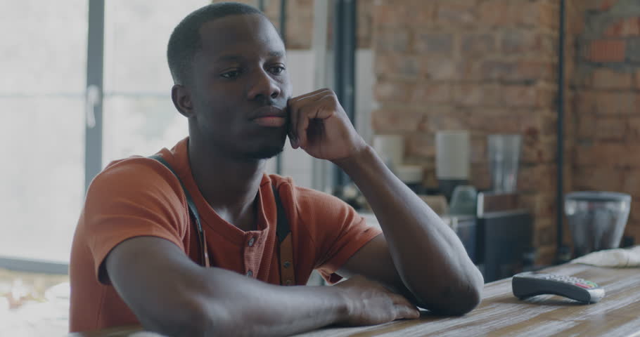 Portrait of pensive African American man barista waiting for customers at counter in cafeteria. Coffee house enployee and small business concept. Royalty-Free Stock Footage #1108466791
