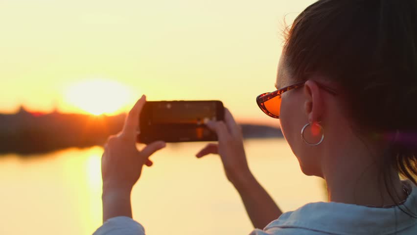 Woman takes photo of sunset sky with mobile phone. Beautiful girl takes pictures and videos of sunset on her smartphone. Idyllic nature landscape panorama Royalty-Free Stock Footage #1108472553