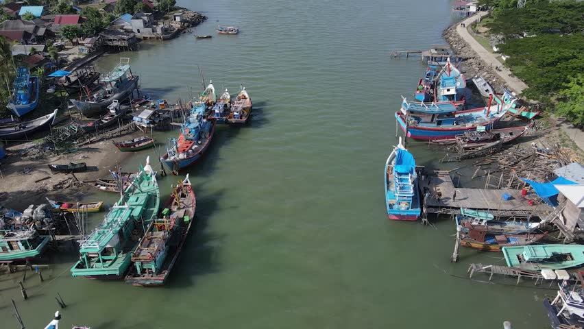 Aerial footage along the river with dozens of fishing boats of various shapes and sizes parked on the side of the river. Fisherman