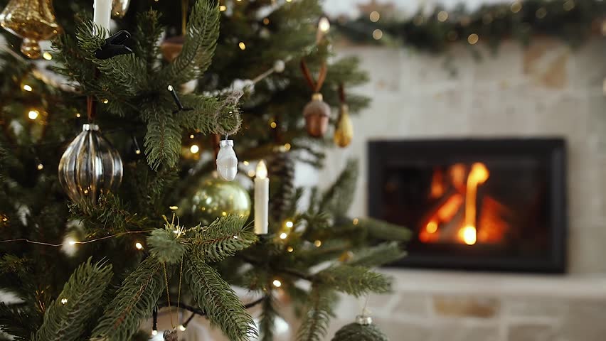 Christmas tree against burning fireplace. Stylish decorated christmas tree with vintage baubles and festive lights on background of fireplace. Atmospheric christmas eve Royalty-Free Stock Footage #1108476233