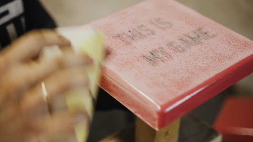 A man licks with sandpaper the surface of a metal bag with the inscription - This is my game. Close-up.
