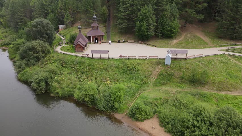 A small chapel sitting on a riverbank surrounded by forest