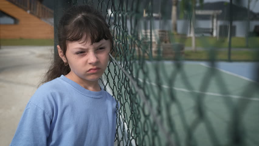 Refugee child alone on the playground. Sad schoolgirl with iron mesh on the playground. The problem of assimilation of a refugee in a new country. Royalty-Free Stock Footage #1108479467