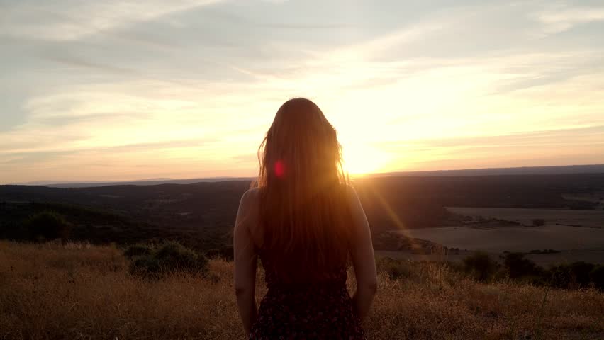 Unrecognizable female traveler opens her arms as a symbol of freedom during a sunset. Concept of travel, freedom