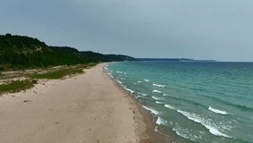 Aerial Drone footage of the Lake Michigan Shoreline in Frankfort. A beautiful sunny summer day with sand dunes, waves, boats, and lighthouses visible.