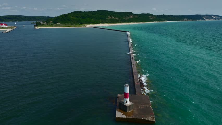 Aerial Drone footage of the Lake Michigan Shoreline in Frankfort. A beautiful sunny summer day with sand dunes, waves, boats, and lighthouses visible.