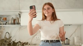 Portrait of European girl teenager in casual clothes taking videocall while spending time in cozy kitchen
