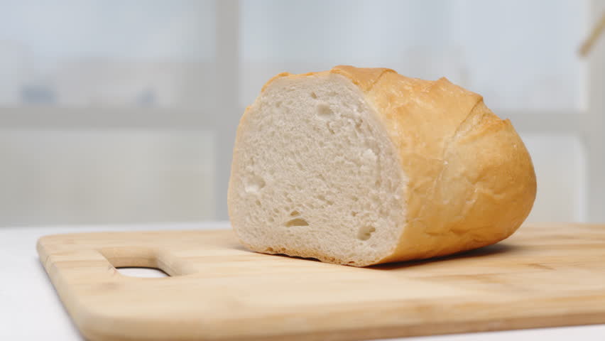 Loaf of white bread on cutting wooden board on light background close-up. | Shutterstock HD Video #1108486475