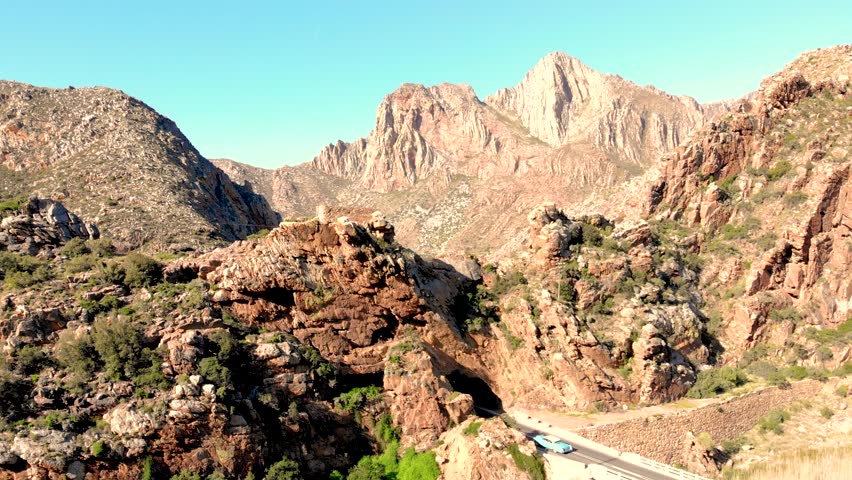 A breathtaking drone perspective follows a winding mountain road, ascending to unveil a captivating vista of endless peaks and an expansive road leading into the distant horizon