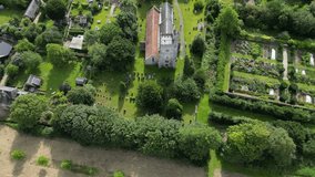A top-down flyover of Holy Cross church in Goodnestone, Kent, with surrounding greenery and cemetery.