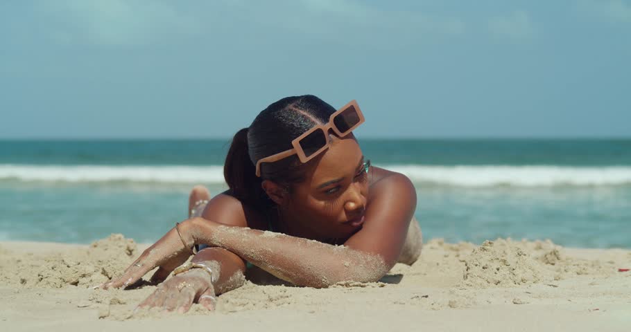Young black girl lays in white sand with ocean waves and blue skies in the background