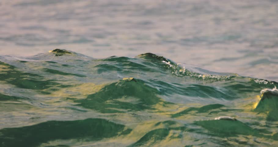 SLOW MOTION CLOSE UP. Top edge of powerful wave breaking and splashing over sandy seashore, water drops spraying in the wind in sunny summer. High quality 4k footage