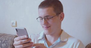 Teenager with glasses sitting on the sofa with a smartphone in his hands.Portrait of a modern person.Close-up.
