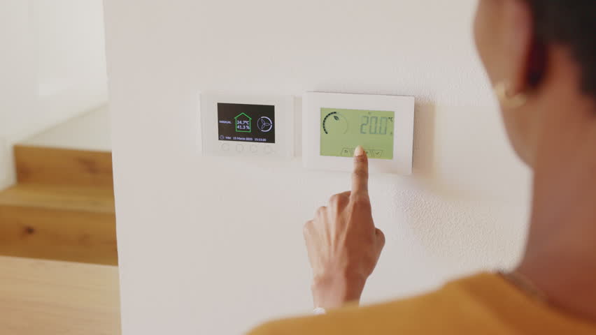 Rear view of multi ethnic woman decrease and set the temperature of a wall attached house thermostat with digital display. Back view of african woman adjusting digital central heating at home. Royalty-Free Stock Footage #1108494241