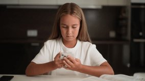 Portrait of adorable kid girl holding smartphone enjoying using mobile apps, playing games sitting at home desk. Small pretty child learning in cellphone, watching video, having fun with mobile phone.