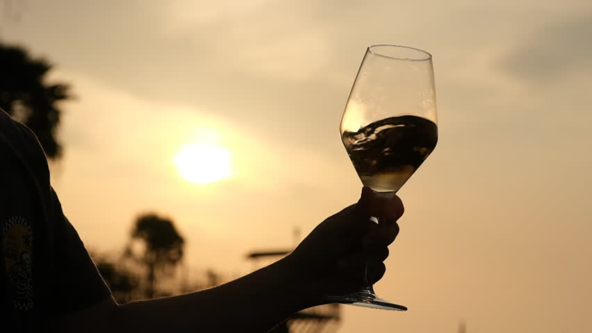 pouring white wine into a wine glass as sunsets, close up, fa01