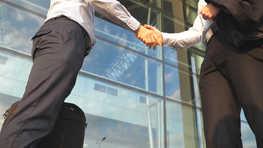 Two businessmen shaking hands of each other near office building then farewell and diverge. Business handshake outdoor in urban environment. Shaking of male arms outside. Close up Slow motion