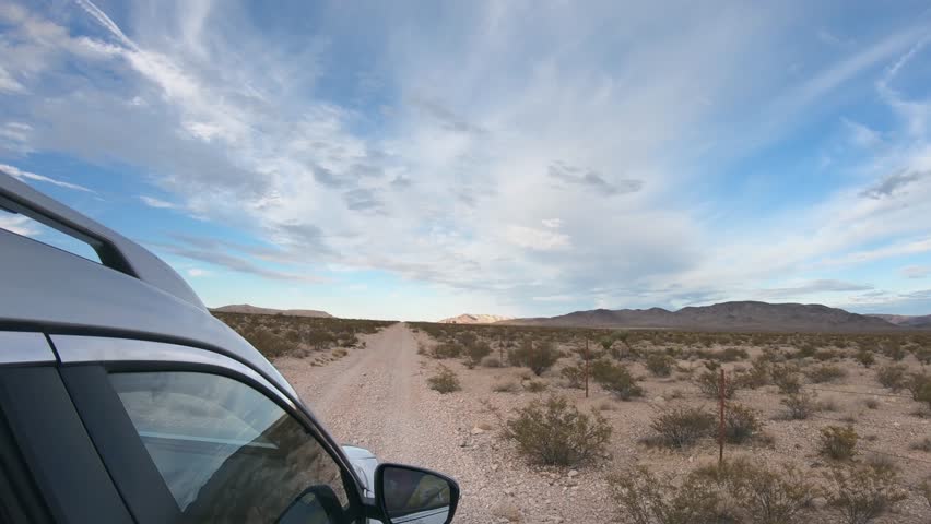 Side view of a car driving offroad through the Nevada desert with sage bushes and dirty road with rocks. Dirty, unpaved road and four-wheel drive on a USA national parks road trip