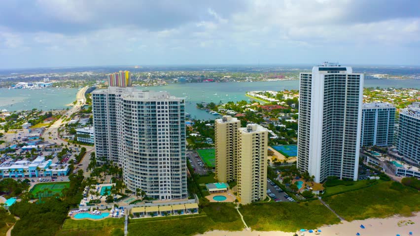 Aerial drone shot slowly rising above the beach on Singer Island looking towards tall residential buildings in West Palm Beach, Florida on a blue sky day. Royalty-Free Stock Footage #1108498821