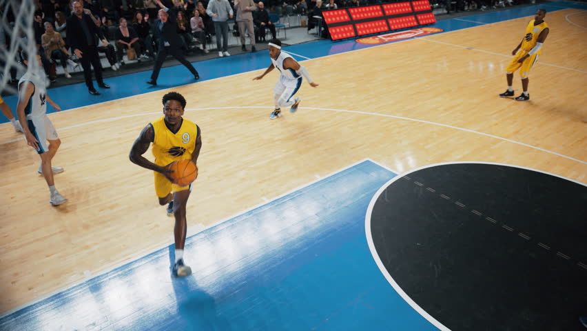 Cinematic College Basketball Tournament: Two Young Successful Diverse Teams Play a Championship Match in a Modern Arena. Excited African Player Scores a Slam Dunk with Two Hands and Hangs on a Hoop