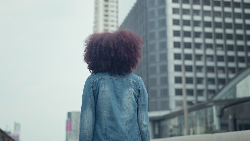 Happy young African American woman with curly hair back and looks at the camera smiling while walking in the street city. Royalty-Free Stock Footage #1108502323