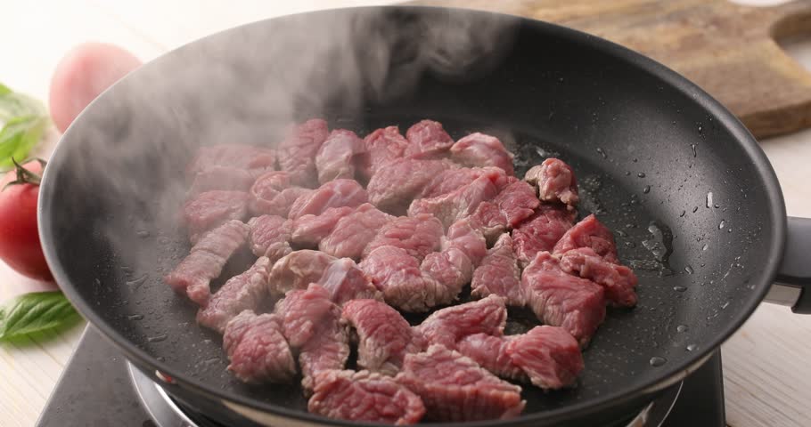 Sliced pieces of raw meat are fried in a frying pan. Roasting beef in a pan. Cooking in the kitchen. Food preparation.