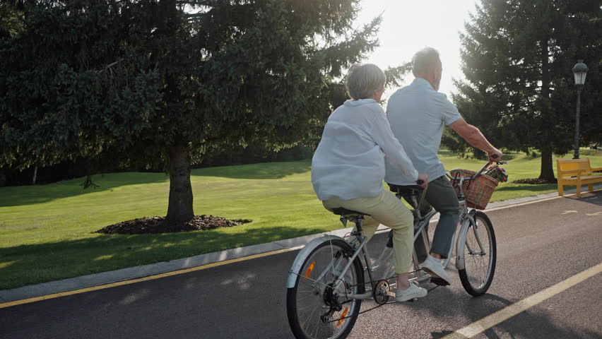 Rear view of fit and healthy husband and wife spending active weekend and riding together on tandem bike. Progressive people dressed in casual wear choosing healthy way of moving around city. Royalty-Free Stock Footage #1108513927