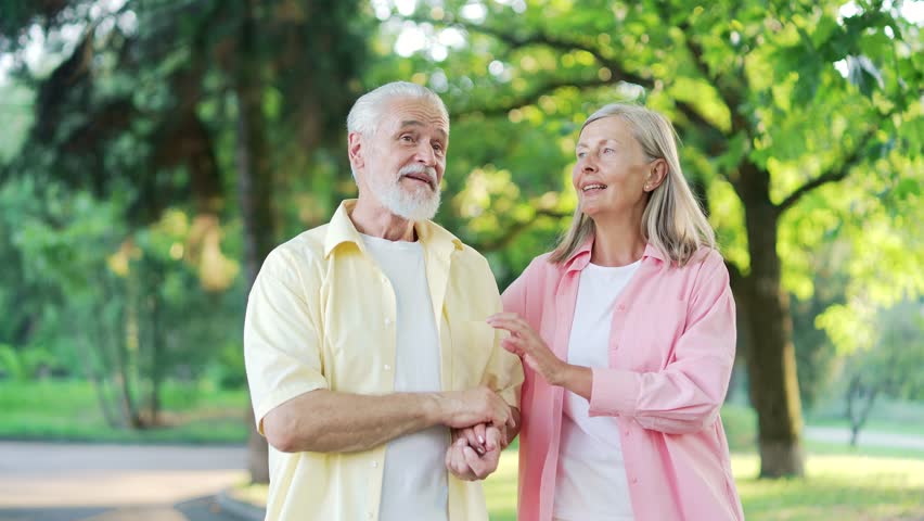 Close up Happy old senior married couple spend leisure time together walking in urban city park. Joyful mature gray haired retired wife and husband have fun talking, hugging, enjoying a walk in nature Royalty-Free Stock Footage #1108515943