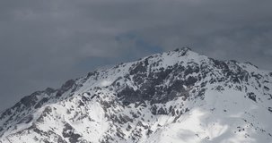 Winter mountains in snow timelapse. Dark gray clouds are flying over snow-covered peak. But in some places sun shines through clouds, and beautiful sun glare runs on snowy peaks. Concept peaceful life