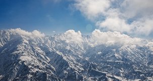 Winter mountains in snow timelapse. Rocky mountain range in the snow under the sun's rays, clouds form right on the slopes. Blue sky. Amazing cinematic background video of Asian nature.