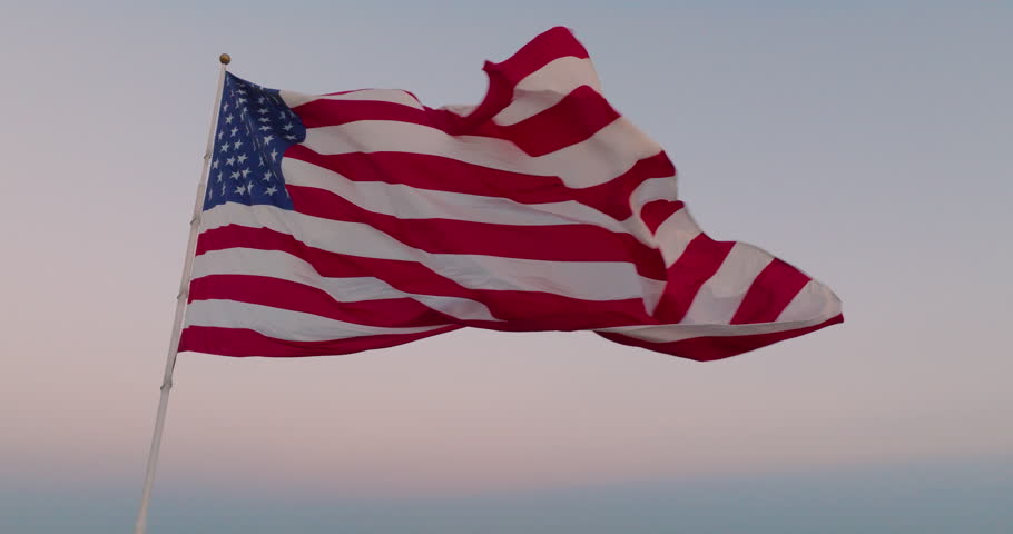Cinematic view of an American flag waving in the wind at dusk as the end of the flag flaps near the camera where the stars and stripes can be seen in beautiful red, white, and blue against the sky. | Shutterstock HD Video #1108524681