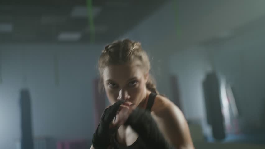 Woman fighter trains his punches and looks at the camera, training in the boxing gym, trains a series of punches fast, front view. Royalty-Free Stock Footage #1108536465