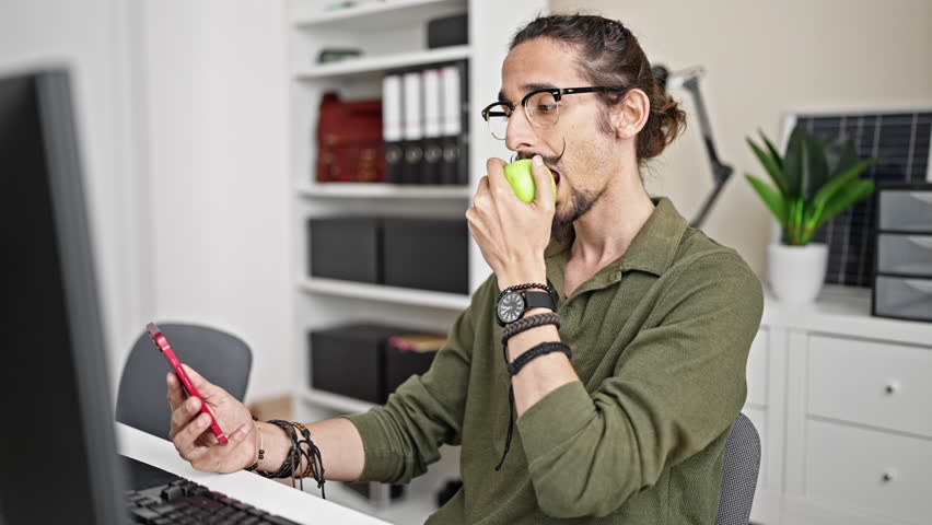 Young hispanic man business worker using smartphone eating apple at office - Powered by Shutterstock - Get 15% off with code: PIKWIZARD15