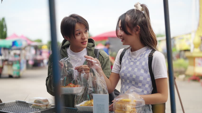 4K Young Asian man and woman buying and eating street food at railway station with using mobile app on smartphone scan QR code making online payment during travel local town on summer holiday vacation