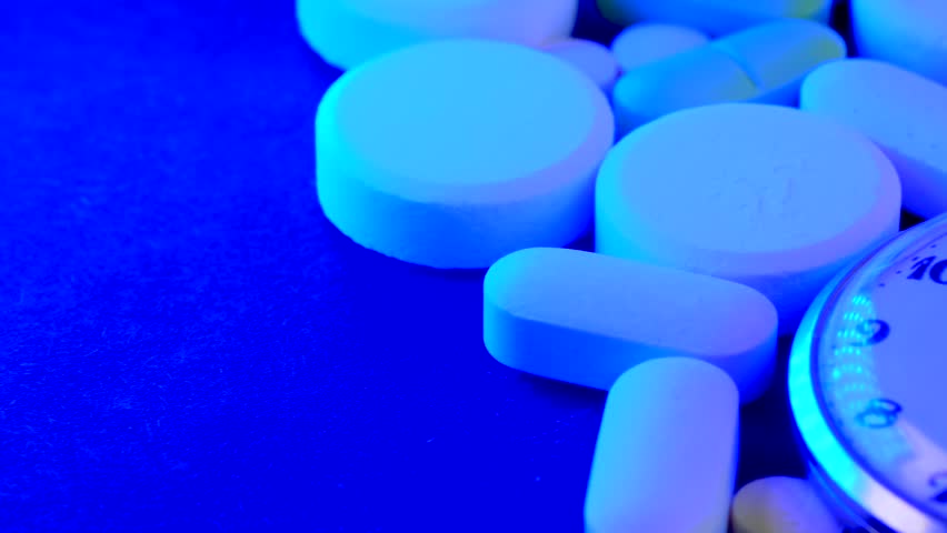 Tracking shot alarmingly flashing blue and red neon lights medicine background with a bunch of drug and different pills with an antique clock showing time of taking medications.