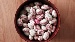 Cranberry beans spinning. Borlotti bean pods in wooden bowl. Top view. Stylish modern food background. Magenta color. Creative foodstuff flat lay. Grocery, dietary backdrop. Advertising, trendy video